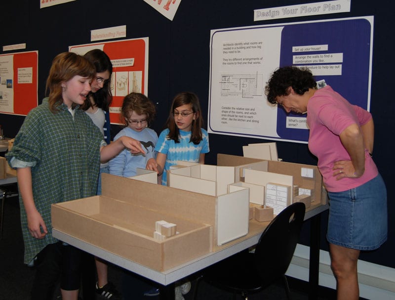Group of children gathered around floor plan display